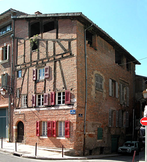 Vielle maison de trois étages, colombages, mur de briques et volets de couleur rouge.